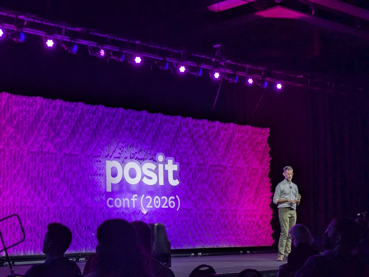 A man stands on stage with a projector screen behind him.