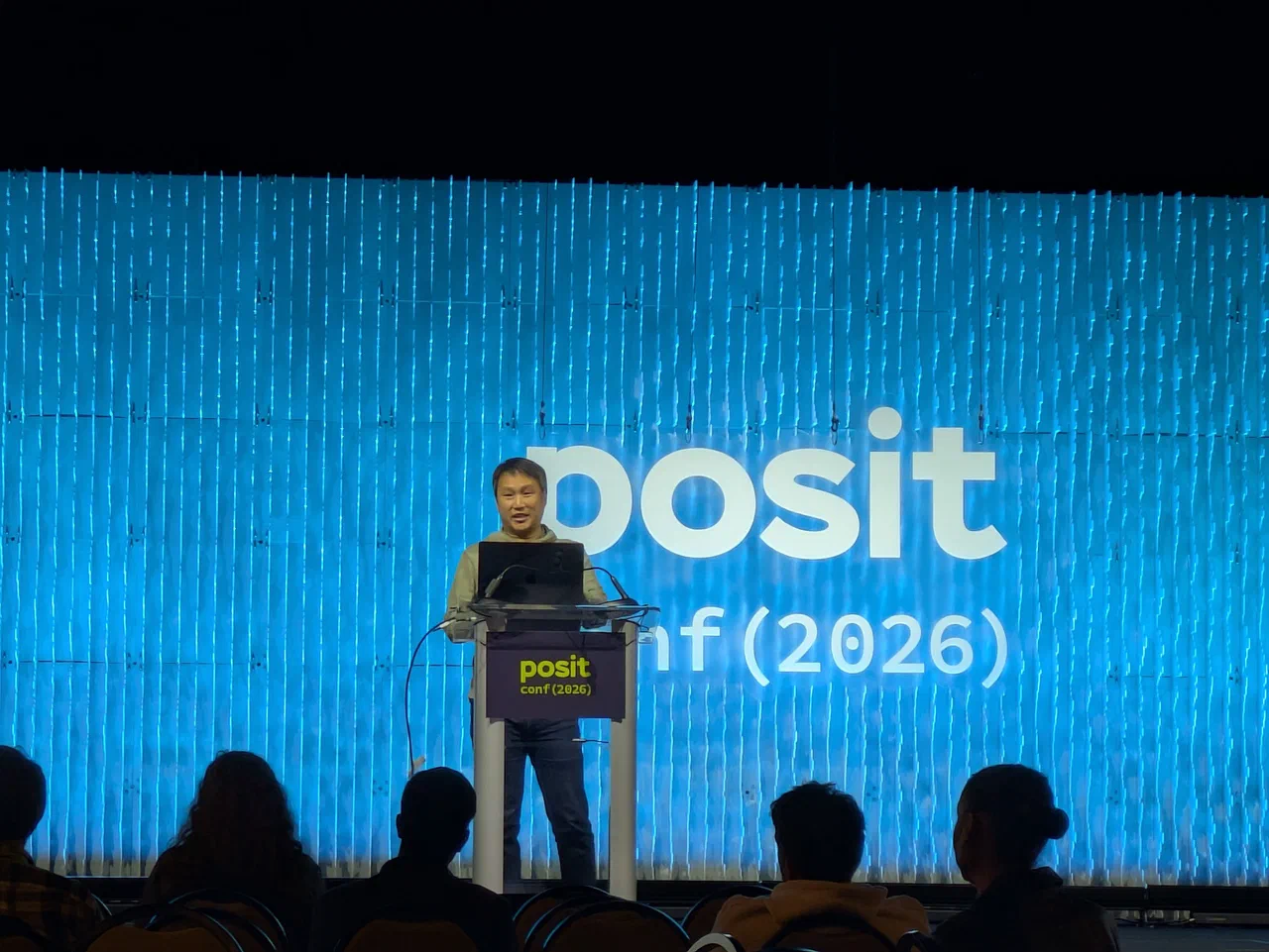 A man stands on stage before a podium and a blue backdrop.