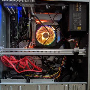 A messy picture of inside of a computer case showing a spinning RGB lit fan cooling a cpu and a tangle of cables.