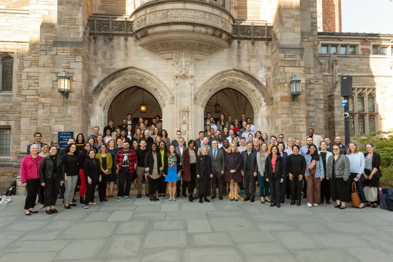 Group photo of approximately seventy people, including attorneys, advocates, policy experts, and state supreme court justices, gathered in front of a stone building with arched entrances at Yale. The group convened to discuss 'Budgeting for Justice: Fiscal Policy and Monetary Sanctions.'