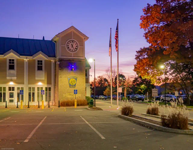 Exterior view of a police station at dusk, with an American flag and the town's seal visible on the building.