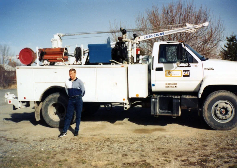 A photograph shows a man standing beside a white CAT service truck with an attached crane. The image illustrates the author's father, a field mechanic, and his truck used to repair heavy equipment in remote areas of Montana.