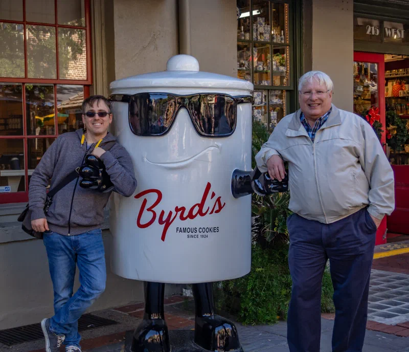 A photograph shows two men, one younger and one older, posing with a large cookie jar shaped like a head. The caption identifies them as the author's father and himself, taken in Savannah in 2018.