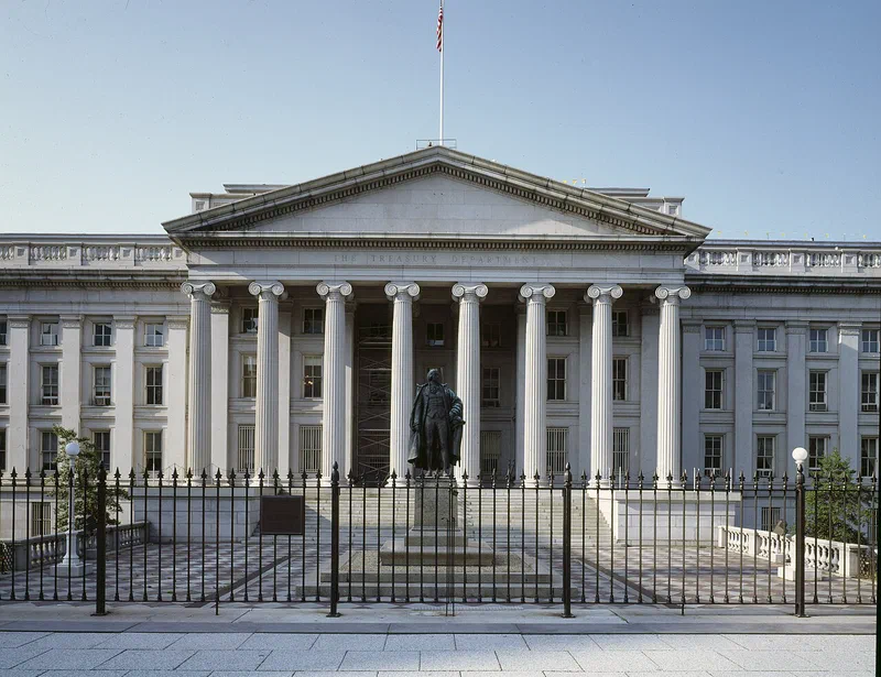 The south portico of the U.S. Treasury Department building in Washington, D.C.: eight white Ionic columns under a pediment carved THE TREASURY DEPARTMENT, with a bronze statue of Albert Gallatin behind an iron fence in front.