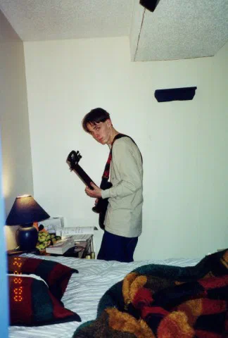 A photograph shows an awkward teenage boy standing in a bedroom holding an electric guitar.