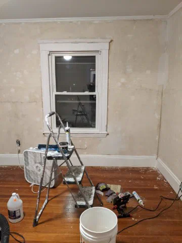 This photograph shows a partially renovated room with freshly plastered walls, a window, and construction tools including a ladder, fan, and paint bucket. The image reflects Civilytics' sentiment that they are 'a work in progress' as they close out 2020.