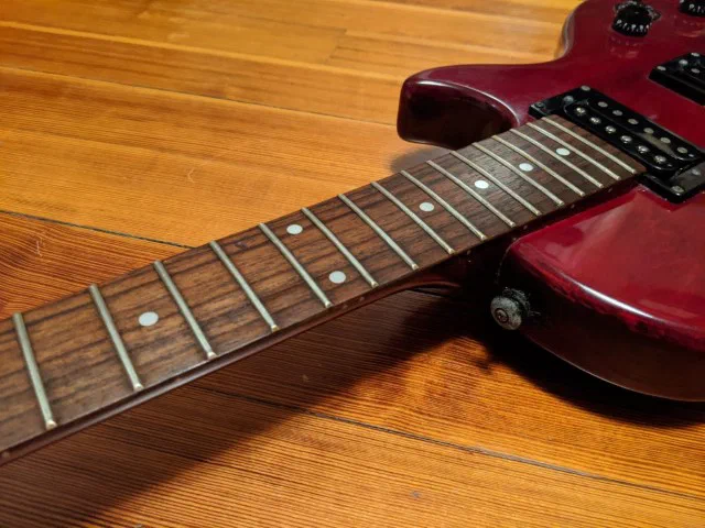 A red guitar with strings removed lays on a wood floor.