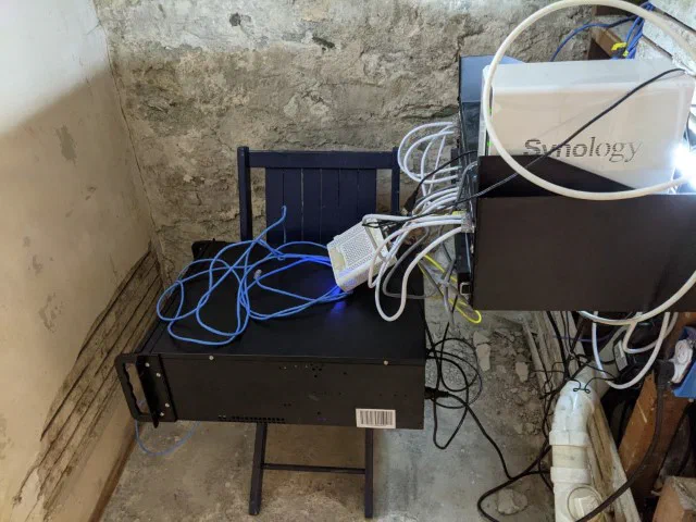 A server rack sits on a black metal shelf in a basement, with networking equipment and cables visible. The setup, described as being behind the washing machine, supports Civilytics' data analysis work on city and county budget reviews.